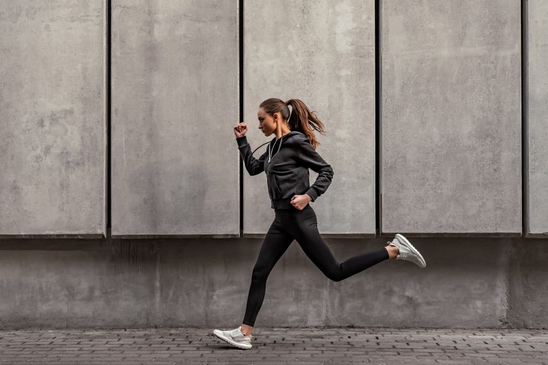 Runner athlete is running near the stadium. Woman jogging workout wellness concept. Side view